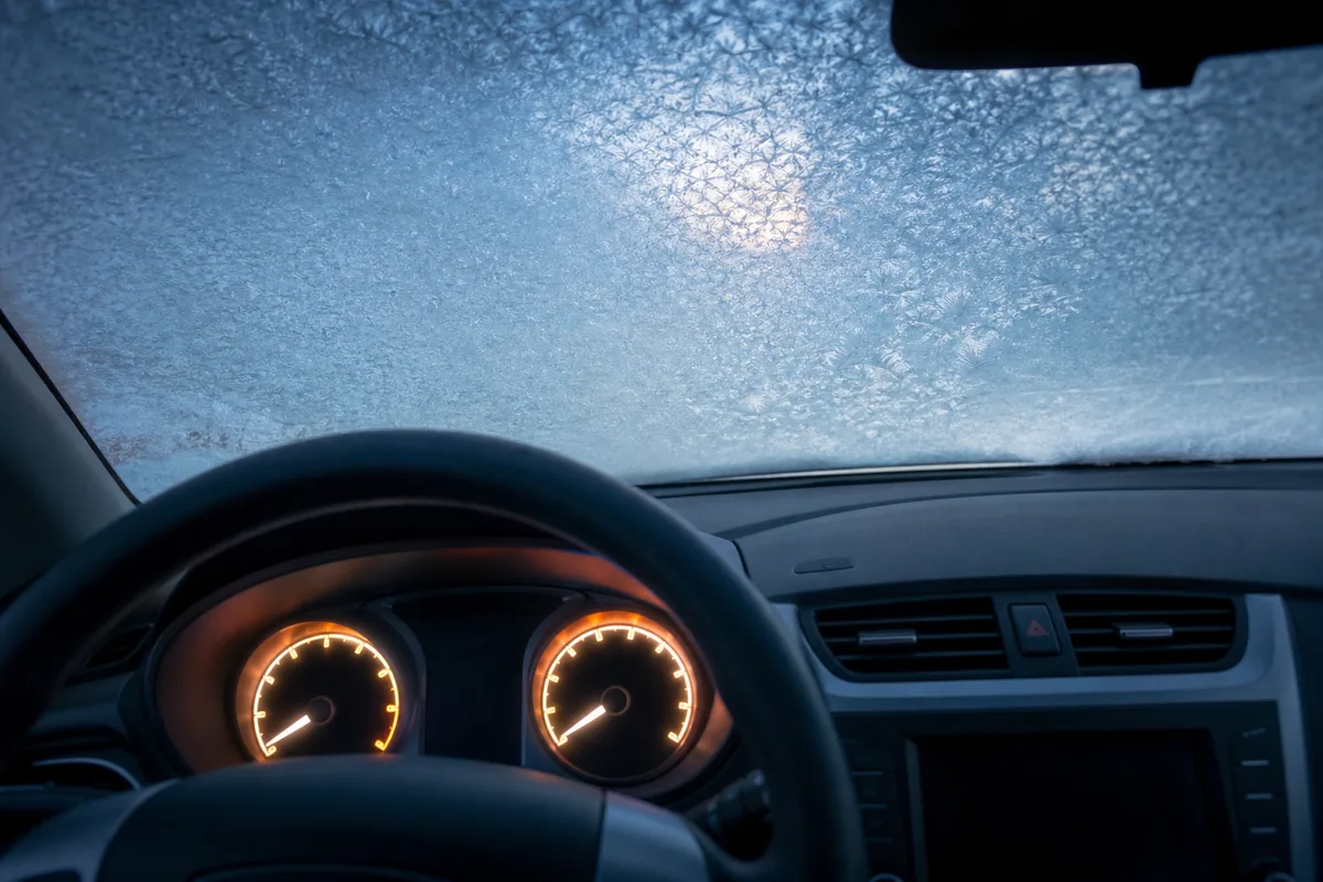 Tableau de bord d’une voiture au démarrage un matin d’hiver, pare-brise couvert de givre