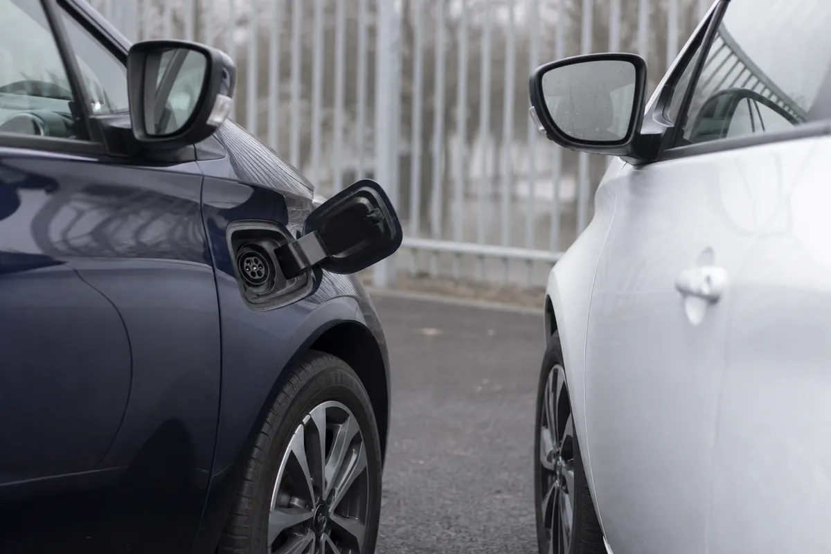 Deux voitures compactes garées côte à côte sur le parking d’un concessionnaire français, trappe de recharge ouverte sur l’une d’elles